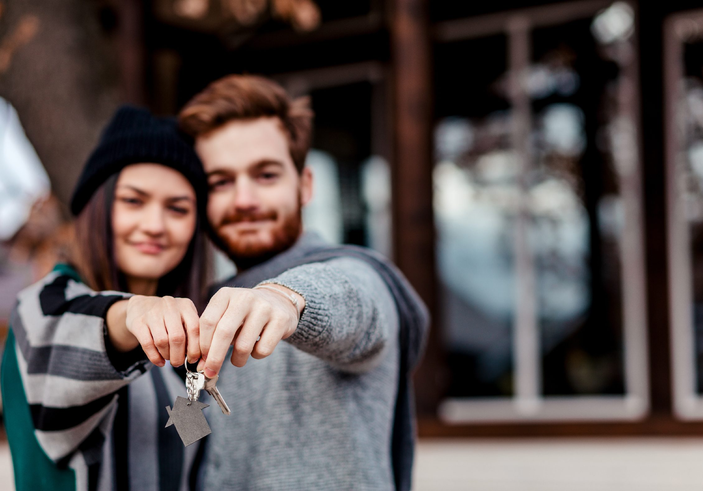 Millennial couple standing side by side holding keys to home smiling